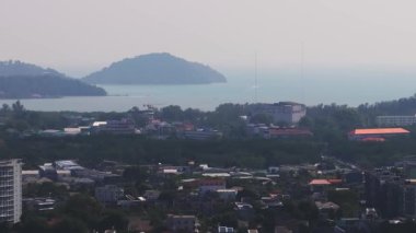 Phuket Adası, Tayland 'ın havadan görünüşü, şehir mimarisi, renkli çatılar, yemyeşil alanlar, tepeler ve uzak bir su kütlesi..