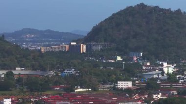 Tayland 'daki Phuket Adası' nın havadan görünüşü yeşil tepeler, bir stadyum, kentsel alanlar, uzak dağlar ve açık mavi bir gökyüzü gösteriyor..