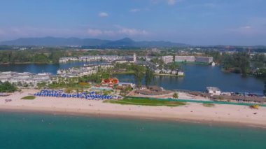 Phuket Adası 'nın havadan görünüşü canlı bir sahil, Tayland tarzı bir bina, dingin bir lagün, yemyeşil, modern binalar ve orman tepelerini gösteriyor..