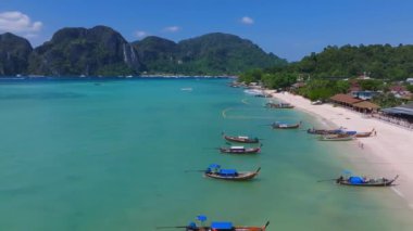 Tayland 'daki Phi Phi Adaları' nın havadan görünüşü turkuaz suları, yemyeşil kayalıklar, küçük kayıklar ve parlak güneş ışığı altında berrak bir gökyüzü gösteriyor..