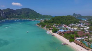 Tayland 'daki Phi Phi Adası' nın hava manzarasında turkuaz sular, beyaz kumlu plajlar, kireçtaşı kayalıklar ve canlı kıyı şeridi yakınlarındaki tekneler yer alıyor..