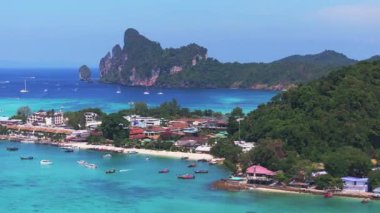 Tayland 'daki Phi Phi Adası' nın havadan görünüşü turkuvaz suları, yemyeşil tepeler, hareketli bir liman, botlar ve tropikal sahil binalarını gösteriyor..
