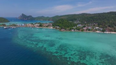 Tayland 'daki Phi Phi Adası' nın havadan görünüşü turkuaz suları, kireçtaşı kayalıkları, kayıklar ve canlı deniz kenarındaki kıyı şeridi yapılarını gösteriyor..