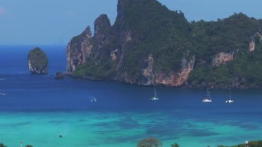 Tayland 'daki Phi Phi Adası' nın havadan görünüşü, yemyeşil tepeler, turkuaz bir koy, küçük tekneler, kumlu bir sahil ve yoğun tropikal bitki örtüsünü gösteriyor..