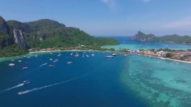 Tayland 'daki Phi Phi Adası' nın hava manzarasında turkuaz sular, yemyeşil tepeler, kireçtaşı kayalıklar, tekneler ve kıyı binaları yer alıyor..