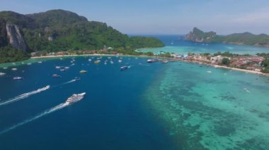 Tayland 'daki Phi Phi Adası' nın hava manzarasında turkuaz sular, yemyeşil tepeler, kayıklar, kireçtaşı kayalıklar ve kıyı tatil beldeleri yer alıyor..