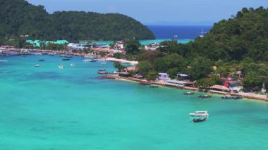Tayland 'daki Phi Phi Adası' nın hava manzarasında turkuaz sular, yemyeşil tepeler, tekneler, kumlu plajlar ve kıyı binaları yer alıyor..