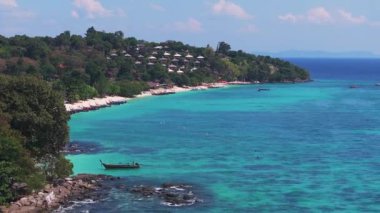 Tayland 'daki Phi Phi Adası' nın havadan görünüşü turkuaz sular, dağınık tekneler, yemyeşil kıyı şeridi ve berrak bir gökyüzü altındaki uzak adalar..