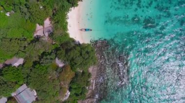 Tayland 'daki Phi Phi Adası' nın havadan görünüşü tenha bir sahil, yemyeşil bitki örtüsü, turkuaz sular, mercan oluşumları ve uzun bir kuyruk teknesi gösteriyor..