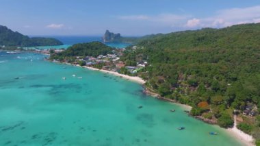 Tayland 'daki Phi Phi Adası' nın hava manzarasında turkuaz sular, yemyeşil tepeler, kireçtaşı kayalıklar, küçük kayıklar ve canlı bir kıyı kasabası yer alıyor..