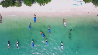 Tayland 'ın Phi Phi Adası' ndaki el değmemiş bir sahil manzarası. Turkuaz sular, uzun kuyruk tekneleri, yemyeşil alanlar ve dağınık plaja gidenler..