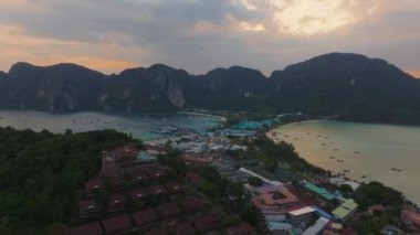 Tayland 'daki Phi Phi Adası' nın havadan görünüşü, verimli kayalıkları, tekneli ikiz koyları, renkli binaları ve sakin bir günbatımı gökyüzünü gösteriyor..