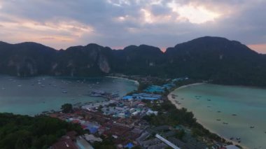 Tayland 'daki Phi Phi Adası' nın havadan görünüşü, kireçtaşı kayalıkları, turkuaz sular, sakin bir koy, dağınık tekneler ve yemyeşil bitki örtüsü sergileniyor..