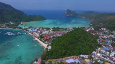 Tayland 'daki Phi Phi Adası' nın havadan görünüşü canlı bir kıyı kasabası, yemyeşil tepeler, kumlu plajlar ve turkuaz sulardaki botları gösteriyor..