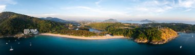 Tayland, Phuket 'teki Naiharn Sahili' nin havadan görünüşü, beyaz kum, turkuaz deniz, demirli tekneler, yemyeşil tepeler ve açık bir gökyüzü altındaki uzak adalar..