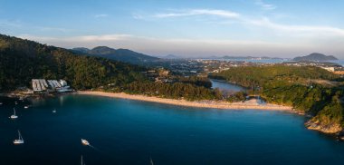 Tayland 'ın Phuket kentindeki Naiharn Sahili' nin hava manzarasında turkuaz sular, demirlemiş yelkenliler, yemyeşil tepeler ve hilal şeklinde kıyı şeridi yer alıyor..