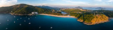 Tayland, Phuket 'teki Naiharn Sahili' nin havadan görünüşü yelkenli, yemyeşil tepeli turkuaz suları ve uzaktaki tepe yapısını gösteriyor..