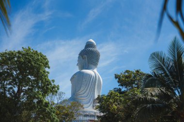 Phuket, Tayland 'daki ikonik Büyük Buda heykeli, ayrıntılı detaylar, yemyeşil ağaçlar ve bulutlu parlak mavi bir gökyüzü ile arkadan görülüyor..