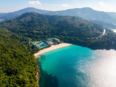 Turkuaz suları olan tenha bir sahil manzarası, yemyeşil tepeler, kıyıya yakın havuzları olan bir tatil köyü ve Tayland, Phuket 'te dolambaçlı bir yol..
