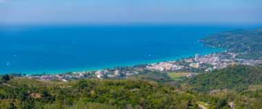 Aerial view of Phuket, Thailand, featuring turquoise waters, white sandy beaches, urban areas near the coast, and lush green hills under a clear sky. clipart