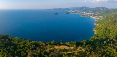Phuket, Tayland 'daki bir kıyı bölgesinin havadan görünüşü, yemyeşil orman, canlı bir mavi koy, kumlu plajlar, küçük bir kasaba ve uzak tepeler..