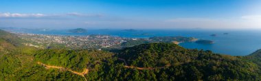 Toprak yolu, Phuket şehri ve Andaman Denizi olan yemyeşil tepelerin hava manzarası. Küçük adalar ve açık mavi gökyüzü sahneyi tamamlıyor..