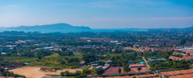 Phuket, Tayland 'ın panoramik hava manzarası, turuncu kiremitli çatılar, yeşil alanlar, dingin mavi bir deniz, uzak adalar ve tepe manzarası.