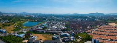 Phuket, Tayland 'ın havadan bakış açısı, bir nilüfer havuzu, kırmızı çatılı binalar, yuvarlanan tepeler, ve temiz bir gökyüzü altında küçük adaları olan bir kıyı şeridi..