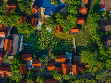 Etrafı yeşilliklerle çevrili Tayland tarzı binalar, nilüfer yapraklı büyük bir nilüfer havuzu ve Tayland 'da kavisli bir yüzme havuzu..