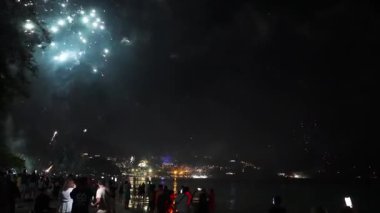 Phuket sahilinde canlı bir yeni yıl kutlaması. Gece gökyüzünü aydınlatan havai fişekler, okyanusu yansıtan ve parlayan bir şehir manzarası..