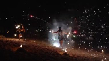 Göstericiler geceleri ateş çukurlarıyla çevrili kumlu bir sahilde yanan copları manipüle ediyorlar. Zayıf ışıklar ve yeşil lazer festival atmosferine ekleniyor..