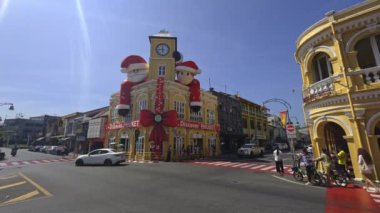 Phuket, Tayland 'da yoğun bir kavşak. Tatil süslemeleri, motosikletleri, arabaları ve yayaları olan sarı bir Sino Portekiz binası var..
