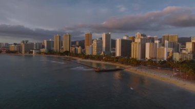 Gün batımında, Honolulu, Hawaii 'deki Waikiki Sahili' nin havadan görüntüsü. Yüksek gökdelenler, okyanus dalgaları ve yemyeşil dağlar sakin bir kıyı manzarası yaratır..