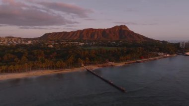 Günbatımında Oahu 'daki Waikiki Sahili' nin havadan temizlenmesi, Elmas Kafa, palmiye ağaçları, kentsel yapılar ve sakin sulara uzanan bir iskelenin yer alması..