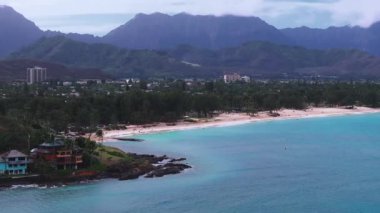 Hawaii, Oahu 'da turkuvaz suları, beyaz kum, yemyeşil yemyeşil ve Ko olau dağlarının kısmen bulutlarla örtülü olduğu bir sahil manzarası..