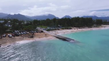 Hawaii, Oahu adasındaki Kailua sahilinin yavaş bir havası, turkuaz suları, küçük bir rıhtım, yakınlardaki evler, yemyeşil alanlar ve dağ sıraları içerir..