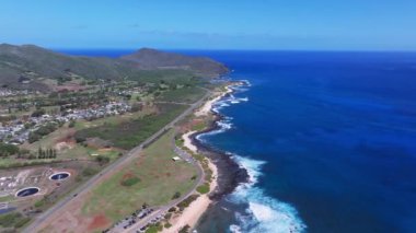 Hawaii, Oahu üzerindeki hava taraması, yerleşim alanları, yemyeşil dağlar, bir otoyol, sahil şeridi, güneş panelleri ve su arıtma tesisleri gösteriyor..