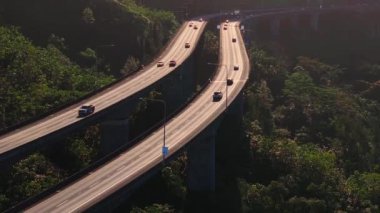 Hawaii, Oahu 'daki yemyeşil dağları kesen eyalet otoyolunun sakin bir görüntüsü. Araçlar yoğun bitki örtüsünün arasında sürekli hareket ederler..
