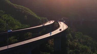 Oahu, Hawaii 'de, yoğun bitki örtüsü ve sıcak güneş ışığı altında hareket eden arabalarla köprülerde yükselen sakin bir eyalet otoyolu manzarası..