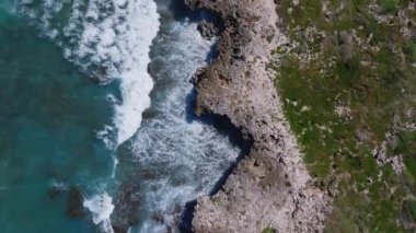 Oahu 'nun turkuaz dalgaların kıyıya çarptığı kayalık sahil şeridinin havadan görüntüsü. Bir kişi patikanın yanında duruyor ve sahneye ölçek ekliyor..