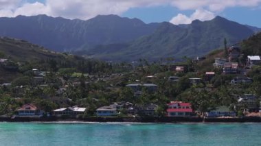 Hawaii, Oahu 'da bir kıyı yerleşim bölgesinin havadan çekilmiş hali. Turkuaz sular, palmiye ağaçları, yamaçtaki evler ve arka planda yemyeşil dağlar..