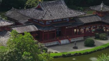 Hawaii, Oahu 'daki Byodo Tapınağı' nın sakin hava manzarası, kırmızı ahşap yapılar, sakin gölet yansımaları ve patikalar boyunca yürüyen ziyaretçiler..