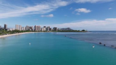 Elmas başlıklı Waikiki Sahili 'nin havadan görünüşü, turkuaz sular, yüzücüler, raket sörfçüleri ve parlak mavi gökyüzünün altındaki Honolulu silueti..