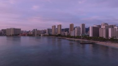 Waikiki Sahili 'nin sakin hava manzarası Honolulu' da yavaş bir tavayla mor gün batımı, gökyüzünü gösteriyor, Royal Hawaiian Hotel, sakin okyanus ve uzak dağlar..