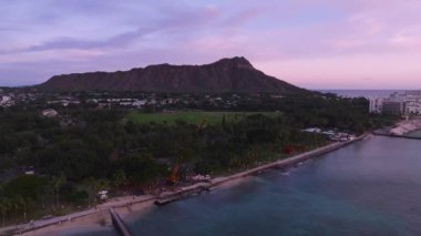 Oahu 'nun kıyı şeridinin sakin hava manzarası, Elmas Kafa, sakin okyanus suları, küçük bir iskele, ve yumuşak pembe gökyüzü boyunca Honolulu yakınlarında binalar..