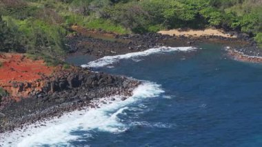 Hawaii 'de Kauai' nin kıyı şeridinin havadan görüntüsü, okyanus dalgalarının koyu volkanik kayalara, kırmızı toprağa ve yemyeşil çimenlere çarpması..
