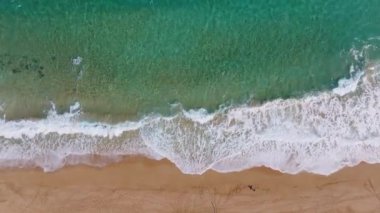 Hawaii, Kauai adasındaki bir kumsalın havadan görüntüsü. Turkuaz dalgalar altın kumun üzerinde akıyor. Yalnız bir insan kıyı boyunca yürür, ayak izleri bırakır..