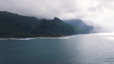 Hawaii 'deki Kauai Adası' ndaki Napali Sahili 'nin hava manzarasında sarp kayalıklar, yemyeşil alanlar, okyanus dalgaları ve kıyı şeridi boyunca yavaş bir tepsi yer alıyor..
