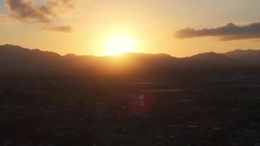 Hawaii 'deki Kauai Adası' nın günbatımında sakin bir hava manzarası. Siluetli dağlar ve küçük bir yerleşim yeri sıcak renklerle ve dağınık bulutlarla çevrili..