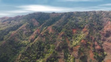 Hawaii 'deki Kauai Adası' nda, parlak, parçalı bulutlu bir gökyüzünün altında yeşil tepeler ve vadilerin üzerinde süzülen hava manzarası. Yoğun bitki örtüsü görünür.